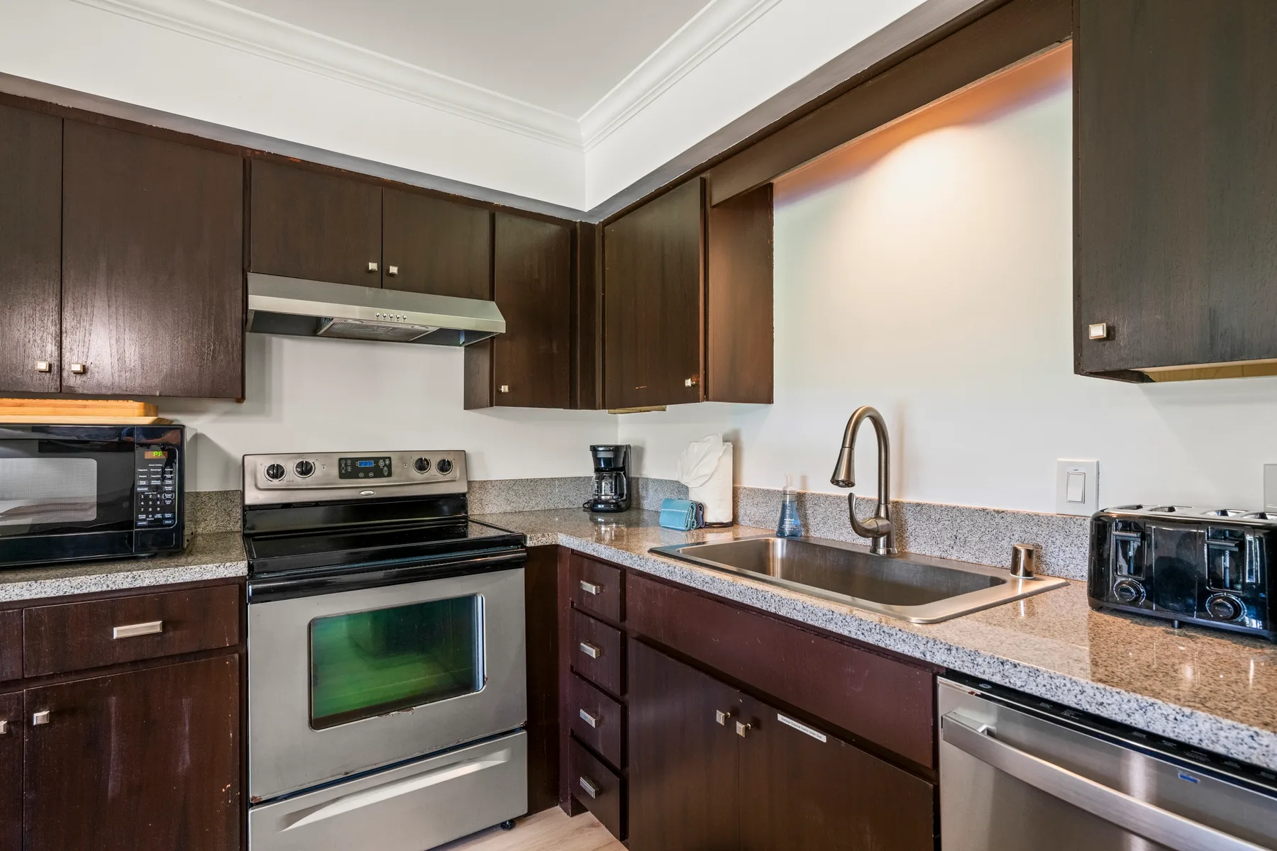A kitchen with dark cabinets, a sink, and stainless steel appliances.