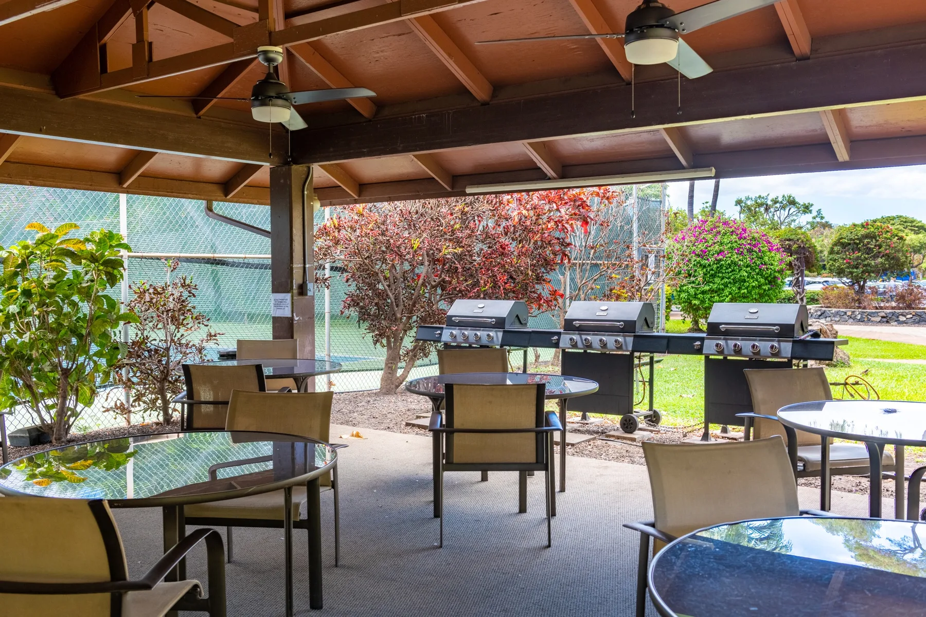 A covered outdoor dining area with tables, seating, and grills overlooking a garden.
