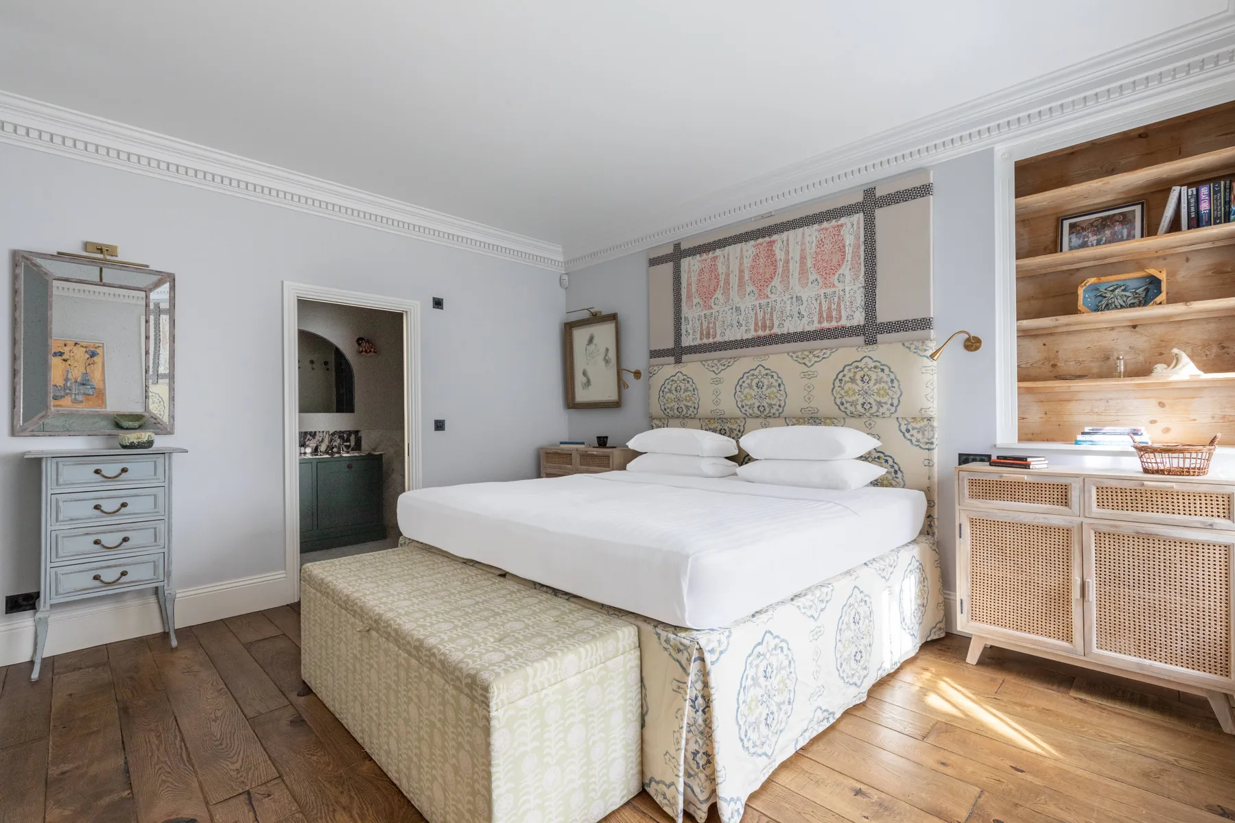 Un dormitorio luminoso con una cama blanca, un cabecero estampado y suelo de madera.