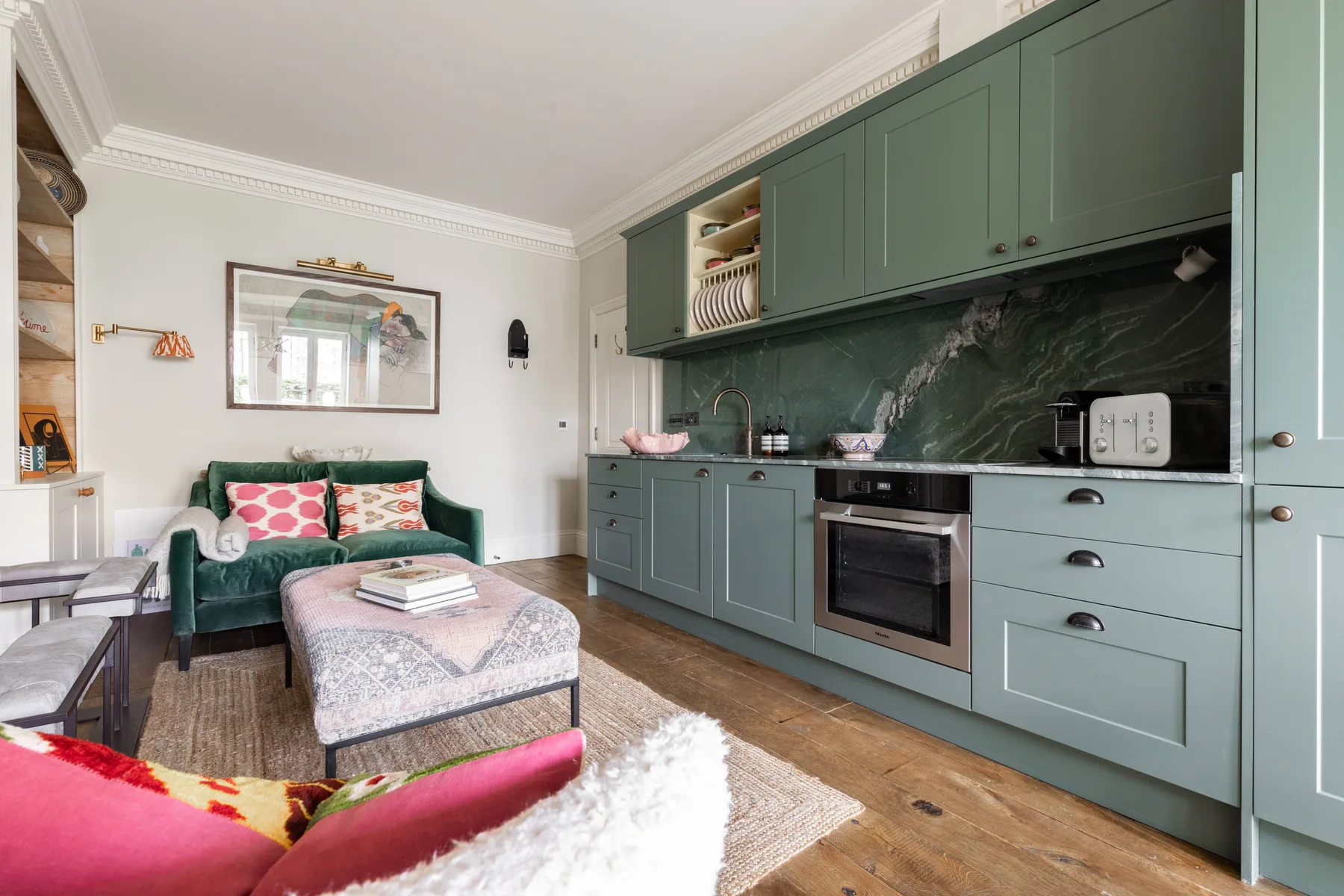 Una sala de estar con un sofá verde junto a una cocina con gabinetes verdes.