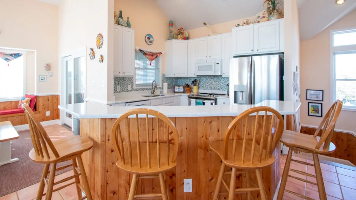 Una cocina luminosa con una barra de madera y gabinetes blancos.