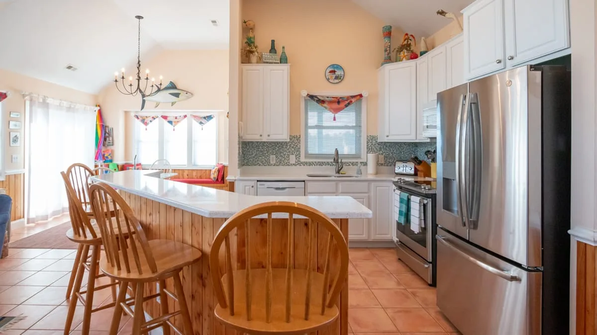Una cocina luminosa con una isla central, asientos de madera y electrodomésticos de acero inoxidable.