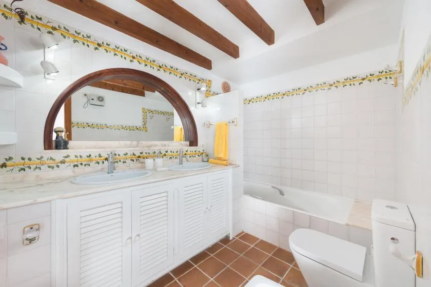 A tiled bathroom with a long vanity, large mirror, bathtub, and toilet.