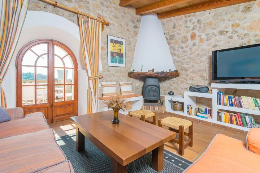 A stone-walled living room with wooden seating and a television.