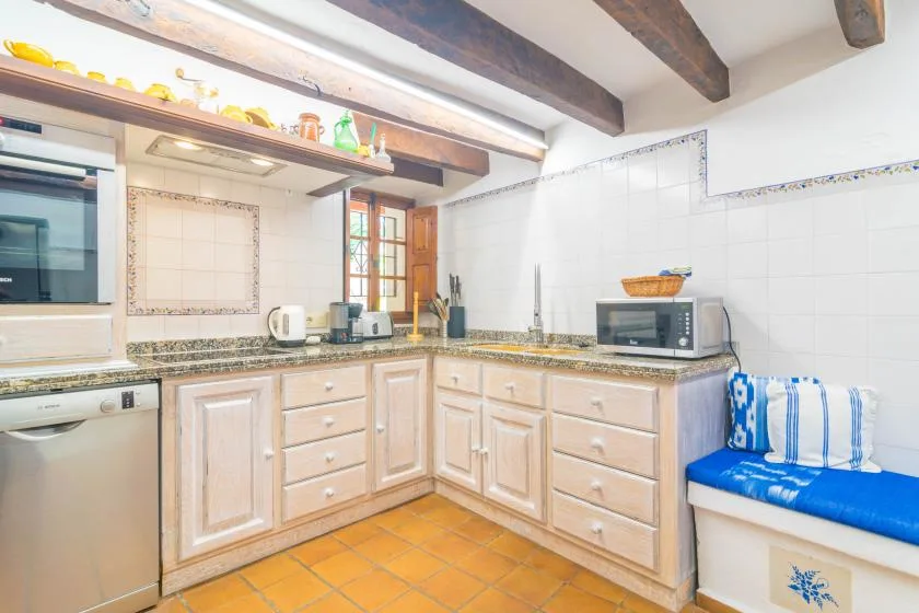 A tiled kitchen with wooden cabinets, countertop appliances, and a blue cushioned bench.