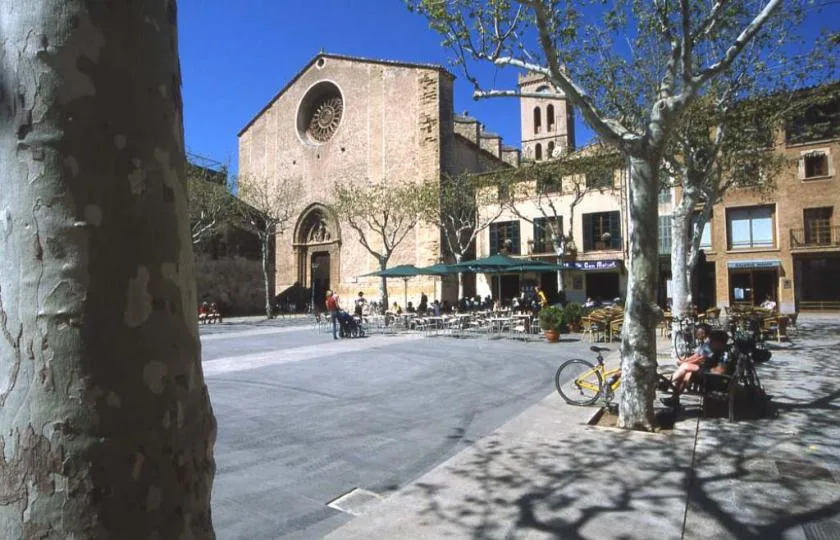 A sunlit plaza with outdoor seating and a stone church in the background.