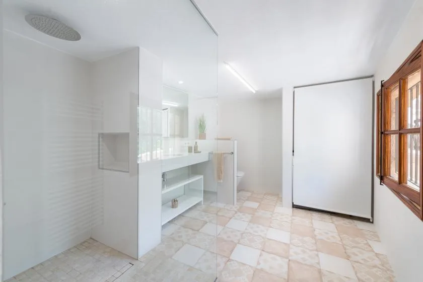 A bright bathroom with a glass shower area, a sink, and a wooden-framed window.