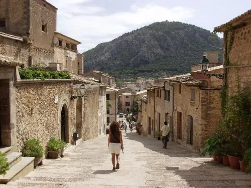 A narrow stone street runs between old buildings toward a wooded hill.