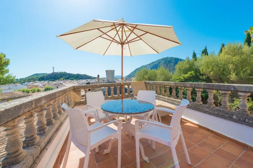 A terrace dining area has a round table and seating beneath a large umbrella.