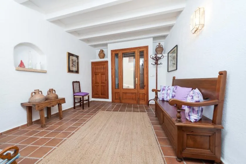 A bright living room with wooden seating, a rug, and a glass-paneled wooden door.