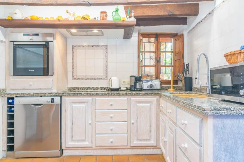 A bright kitchen with pale cabinets, tiled walls, and a counter beneath a window.
