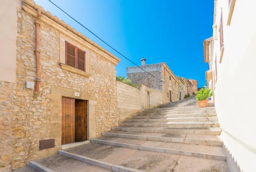 A stone-paved lane climbs between stone buildings under a clear blue sky.