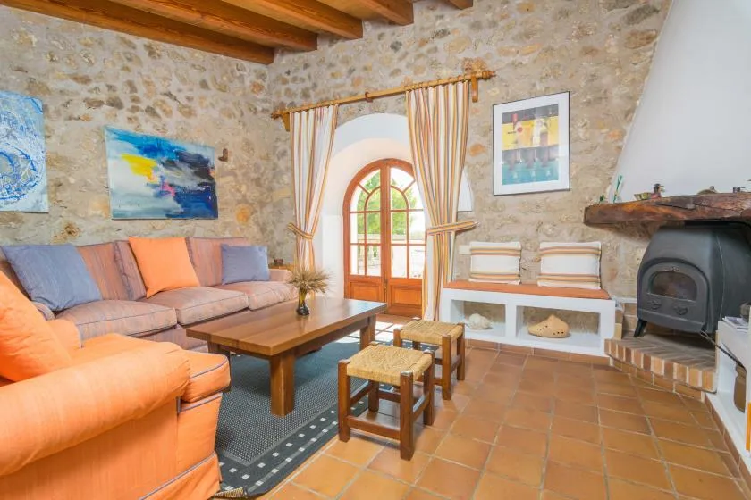 A rustic stone living room with colorful seating, a wooden coffee table, and a fireplace.