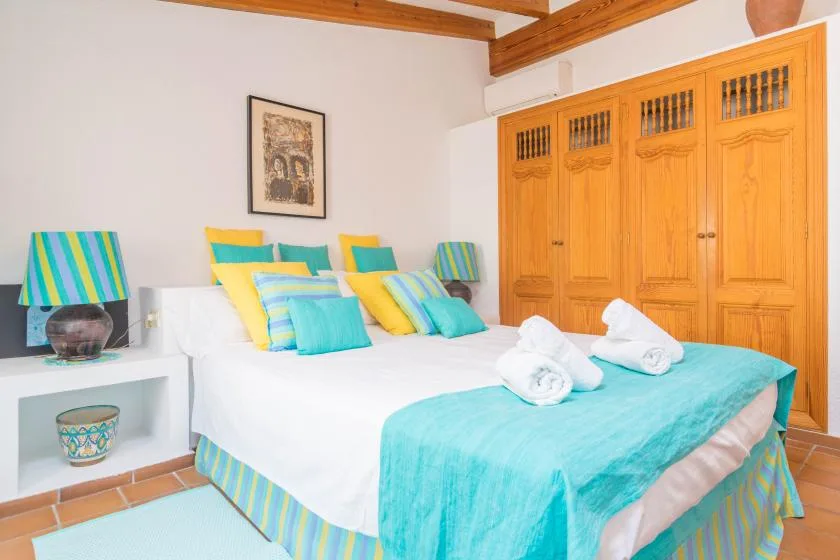 A bedroom with white bedding, turquoise accents, and wooden wardrobes.