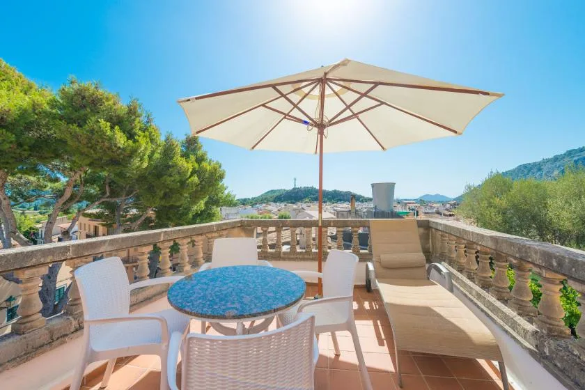 A sunny terrace has outdoor seating, a table, and a large umbrella.