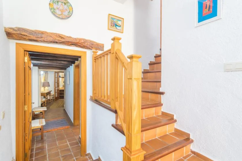 A tiled staircase with wooden railings rises beside a doorway into another room.