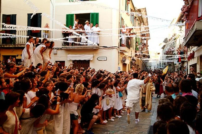 A crowded street procession passes between buildings as spectators line the route.