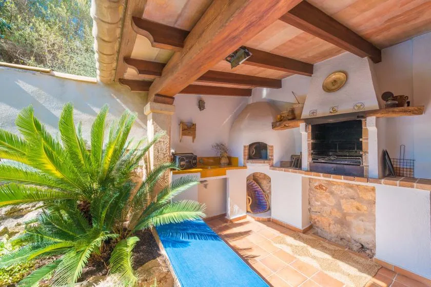 An outdoor kitchen with a built-in grill beside a narrow blue pool.