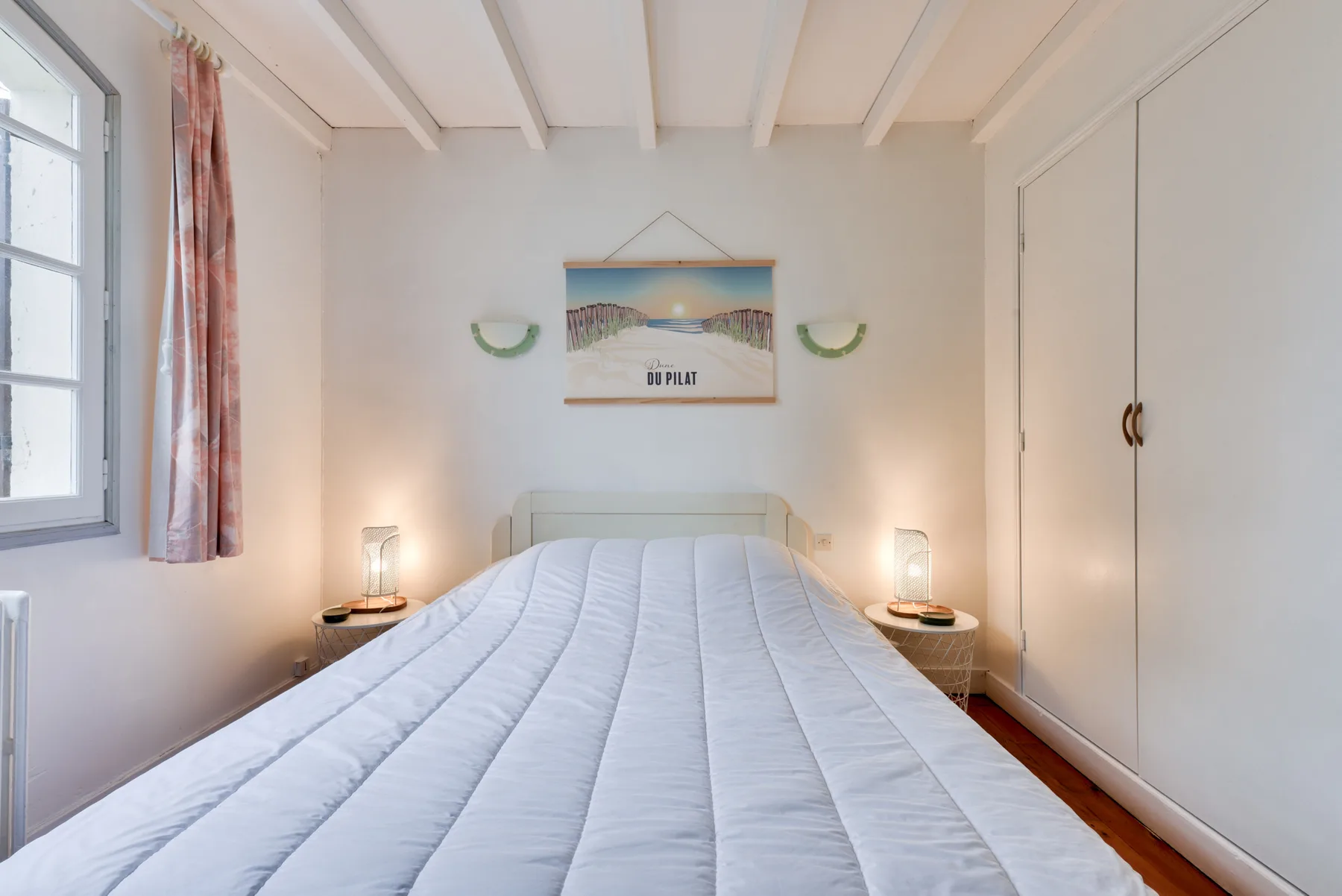 A bedroom with a bed, bedside tables, and a window.