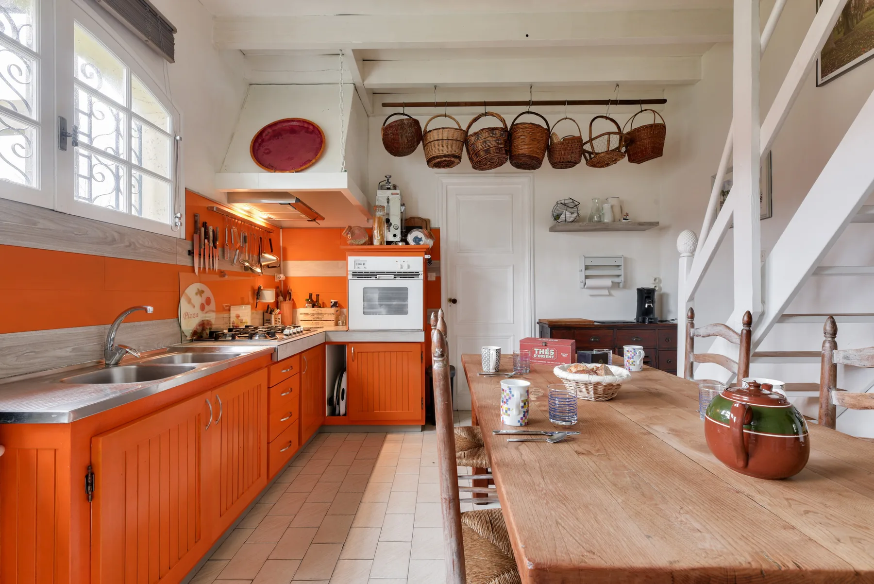 A kitchen with orange cabinets and a long wooden dining table.
