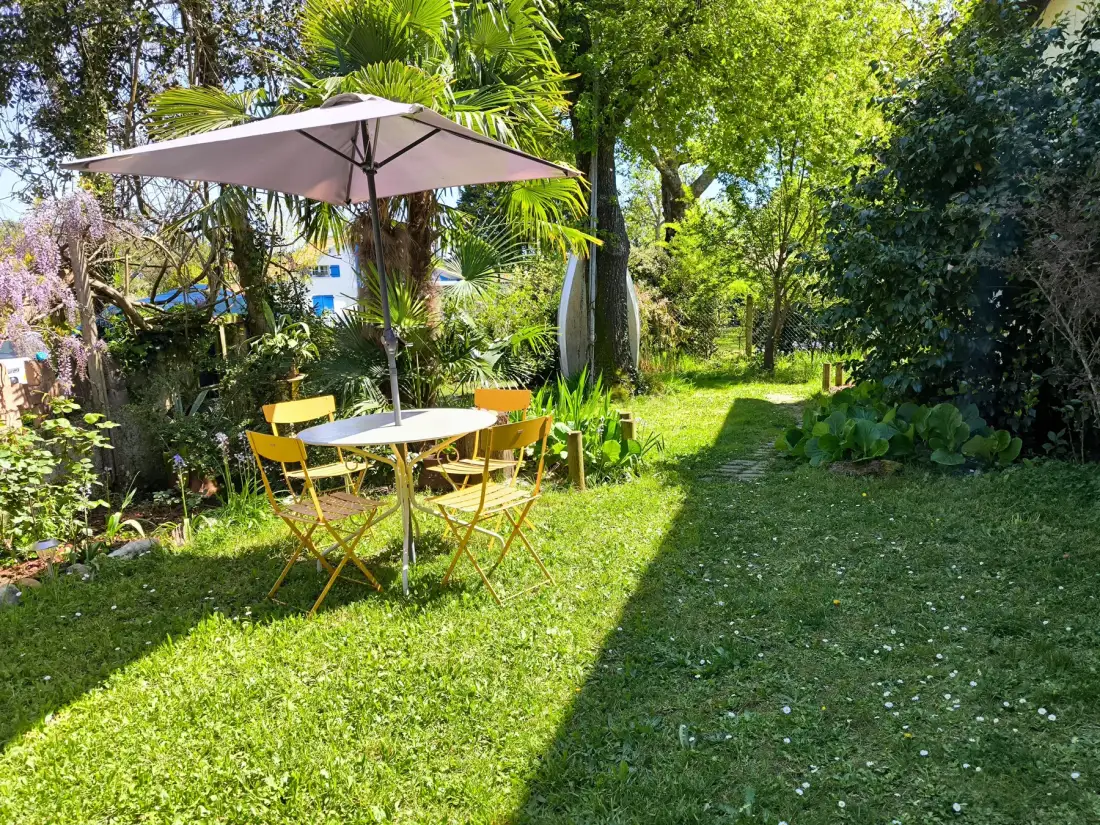 Garden seating area with a table and umbrella among leafy plants.