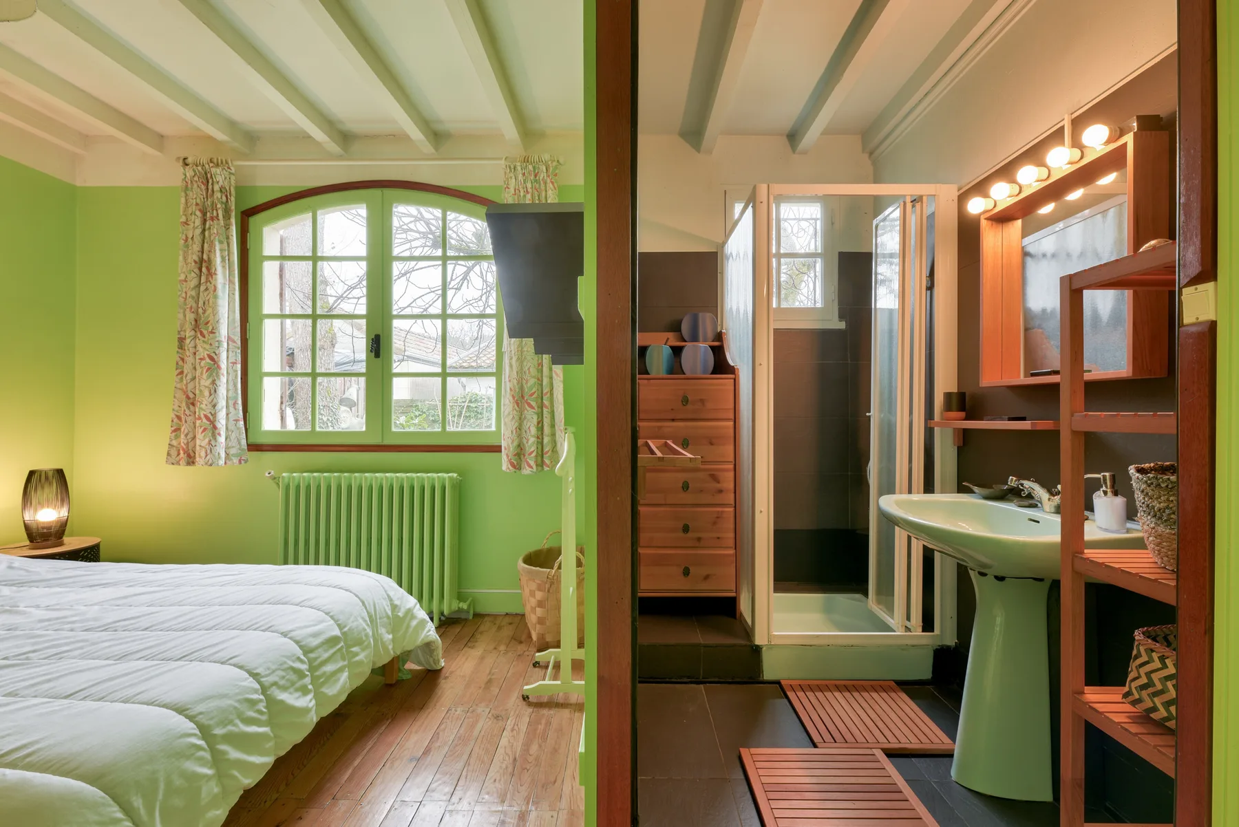 A bedroom with a bed beside a bathroom vanity and mirror.