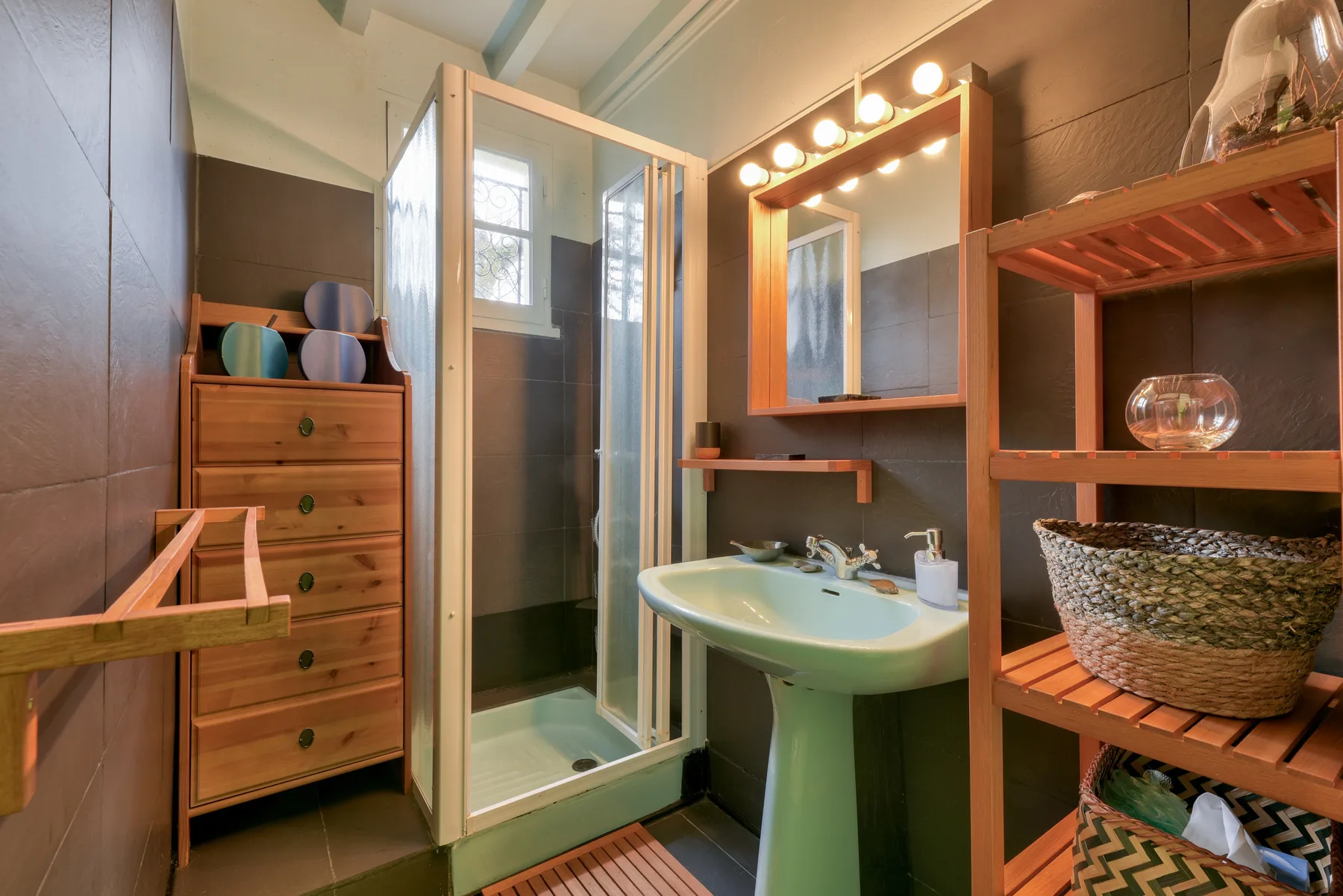 A bathroom with a glass shower, sink, and wooden shelving.