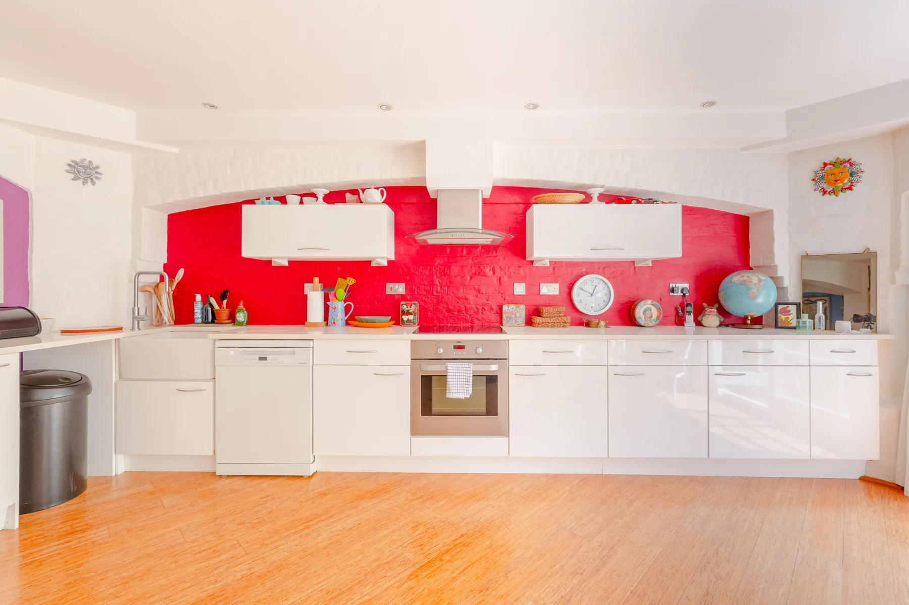 A bright kitchen with white cabinets and a vivid red backsplash.