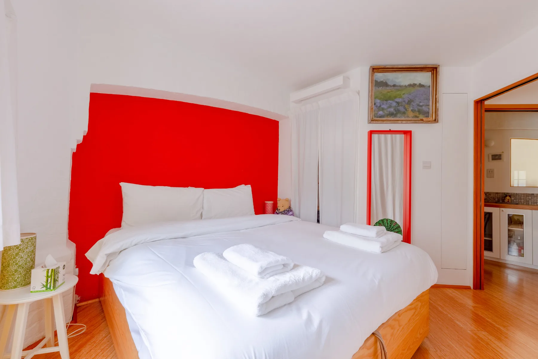 A bedroom with a white bed, bright red headboard, and folded towels.