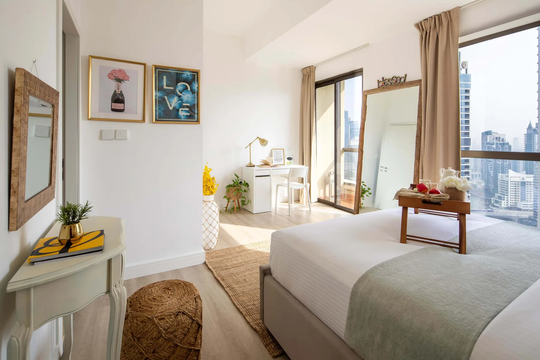 Un dormitorio luminoso con una cama, un escritorio pequeño y grandes ventanas con vistas a la ciudad.