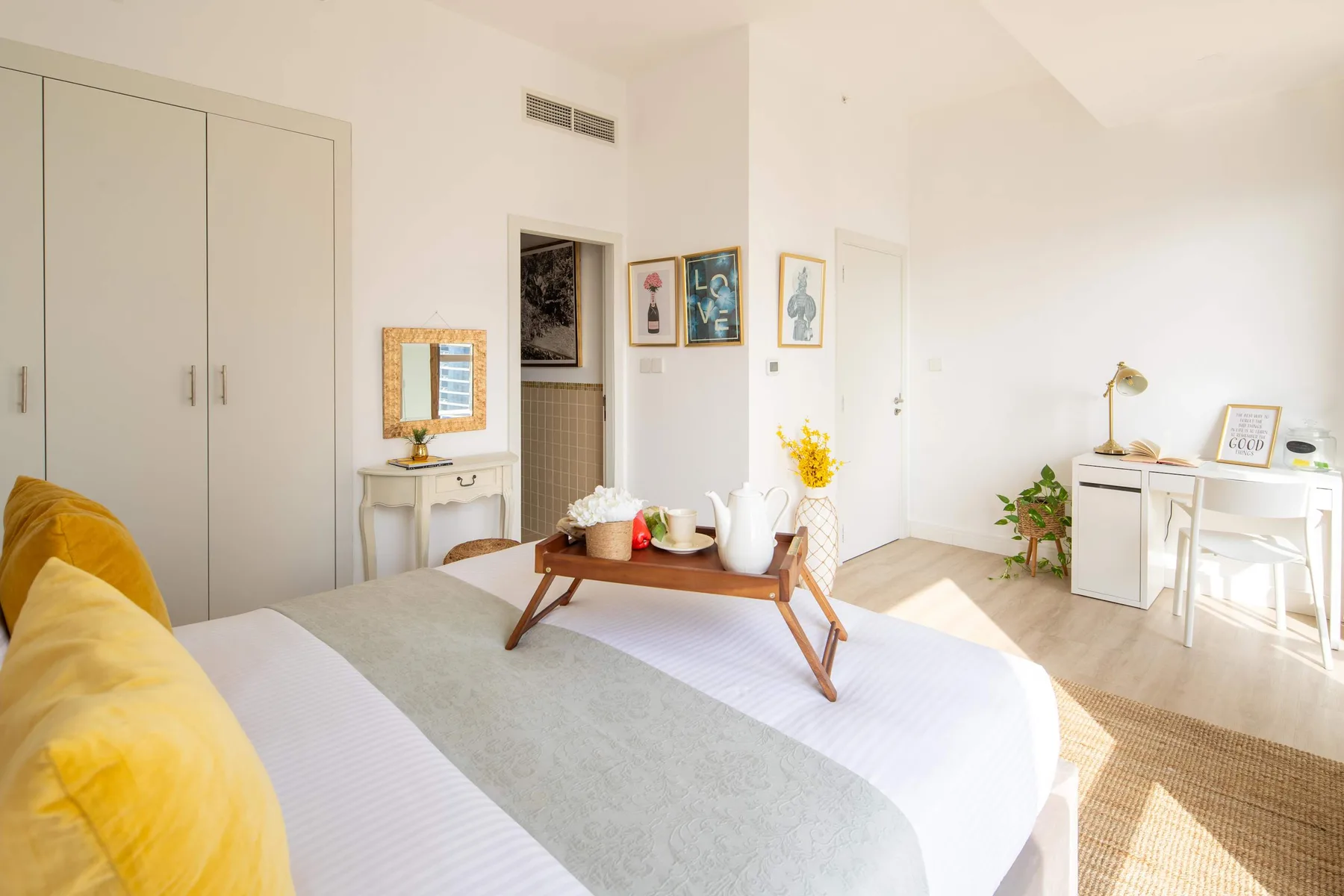 Un dormitorio luminoso con una cama, una mesa baja de madera y un escritorio junto a la ventana.