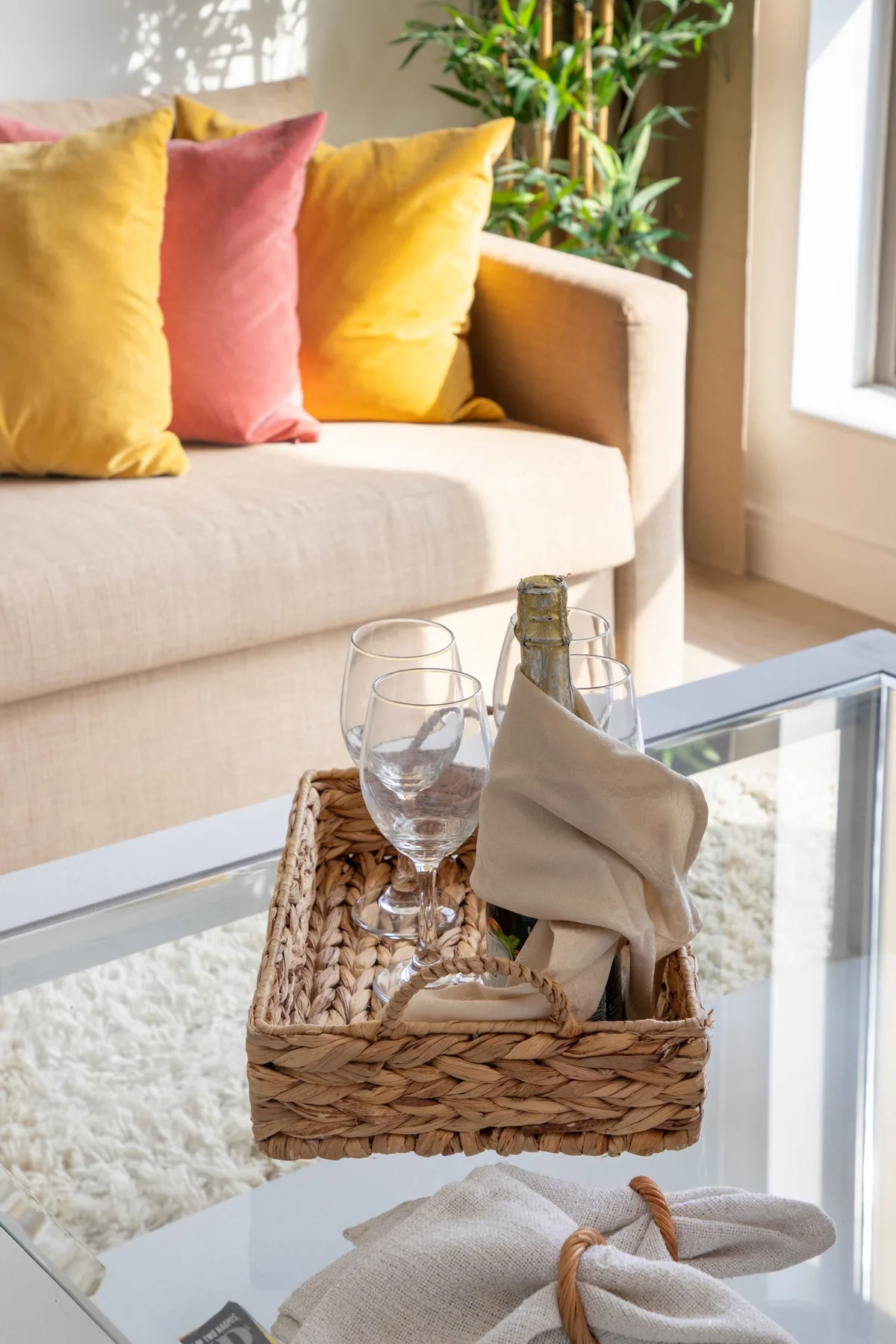Una sala de estar luminosa con sofá, cojines de colores y una mesa de centro de vidrio.