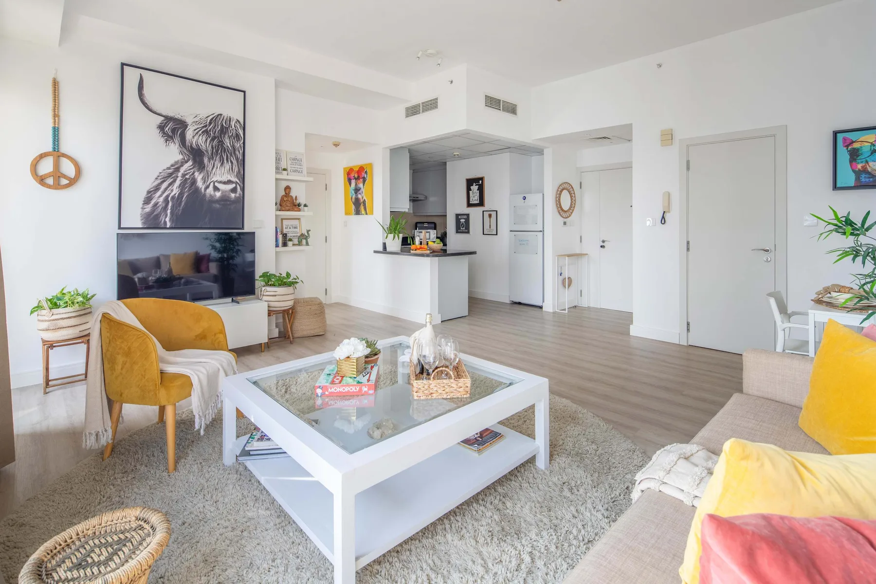 Una sala luminosa con asientos alrededor de una mesa de centro de vidrio y una cocina abierta.