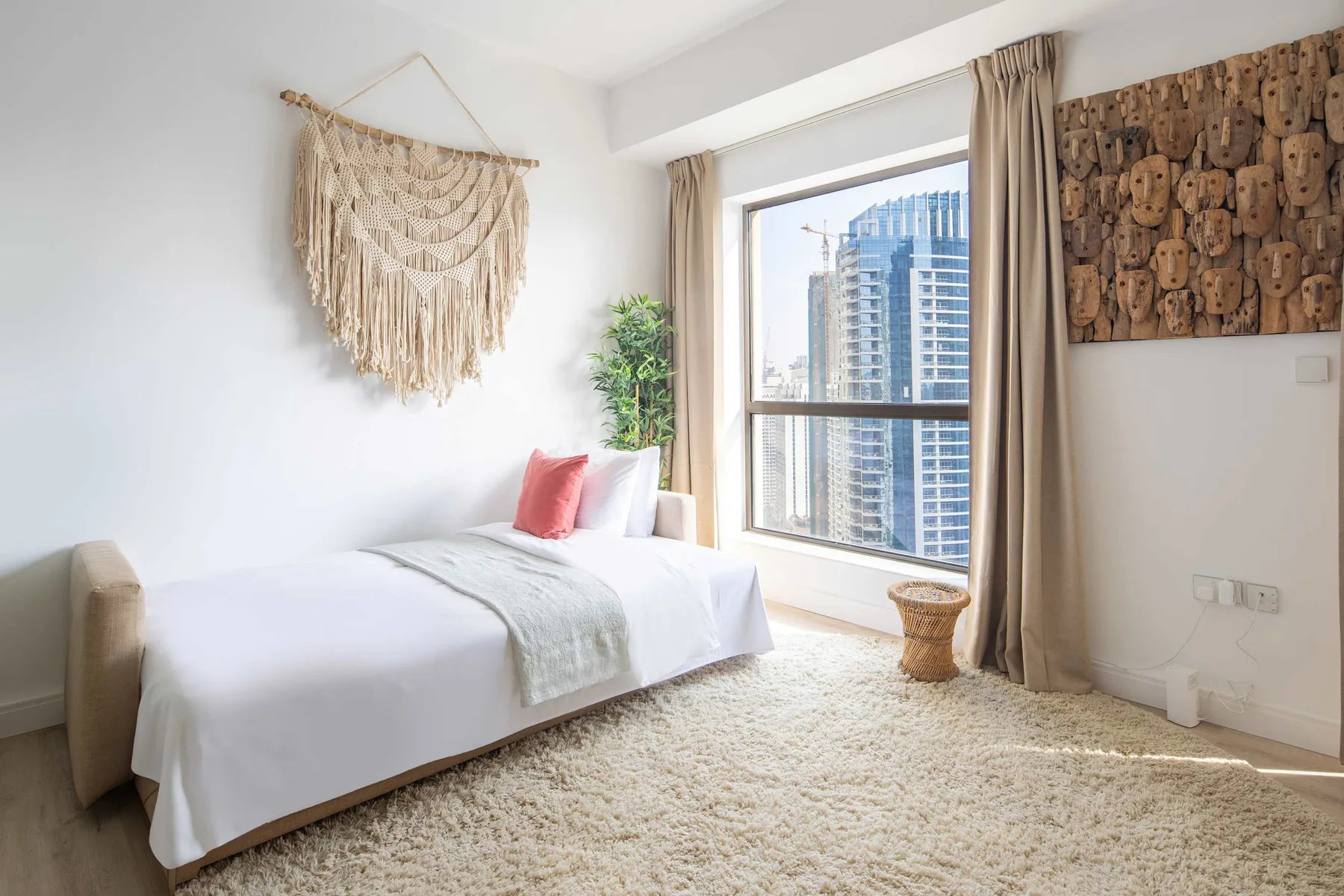 Un dormitorio luminoso con una cama bien tendida junto a una ventana grande.