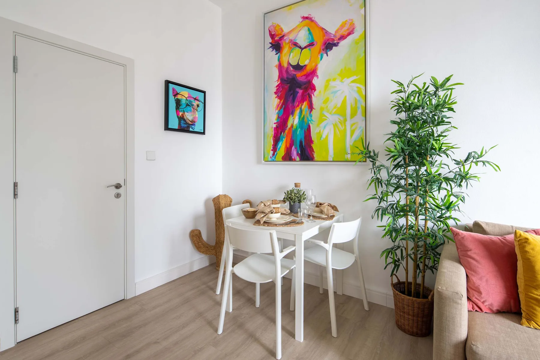Un comedor luminoso con una mesa blanca, arte colorido y una planta frondosa.