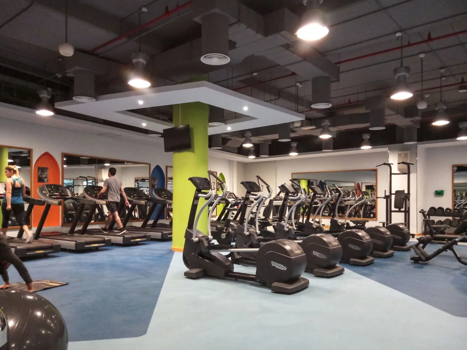Un gimnasio con cintas de correr, bicicletas estáticas y pesas en el suelo.