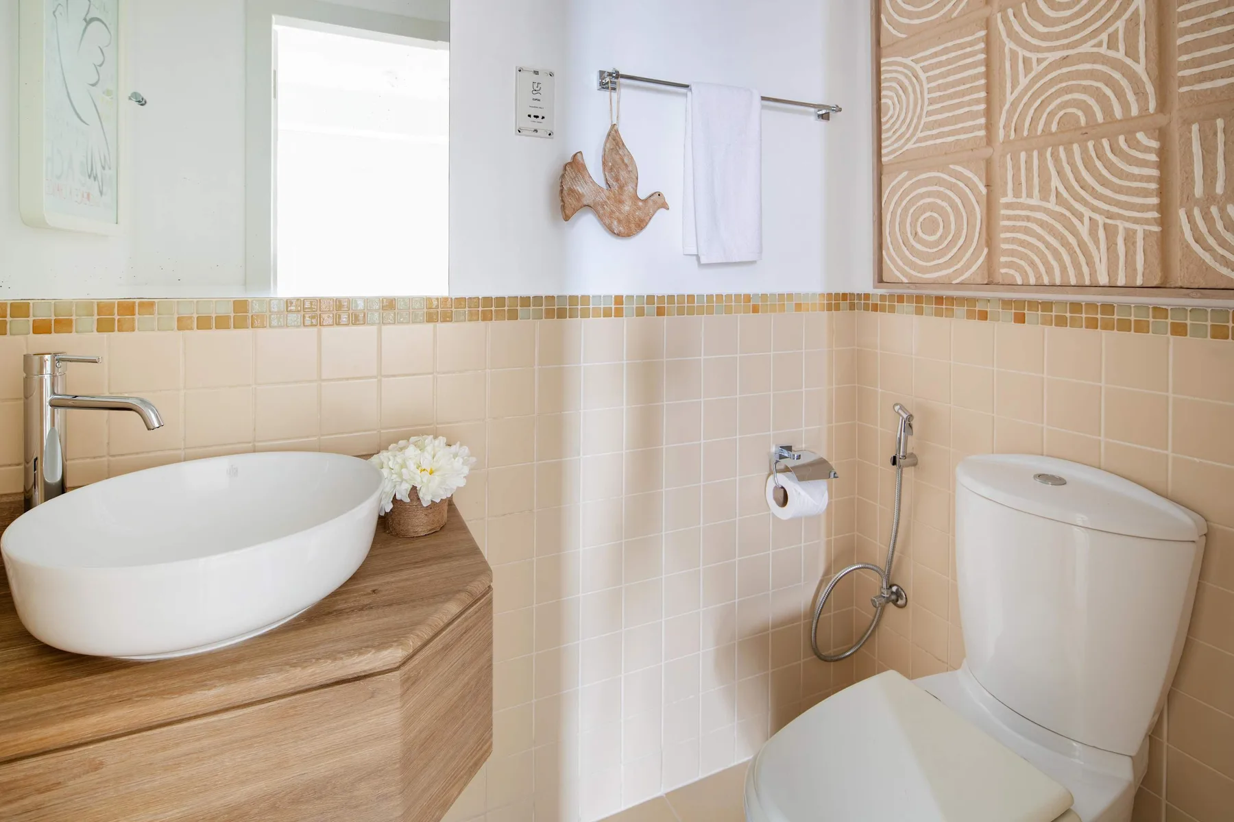 Un baño con azulejos tiene un lavabo sobre encimera, un inodoro y una ducha de mano.