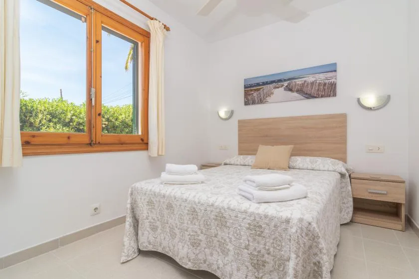 A bedroom with a neatly made bed, bedside tables, and a large window.