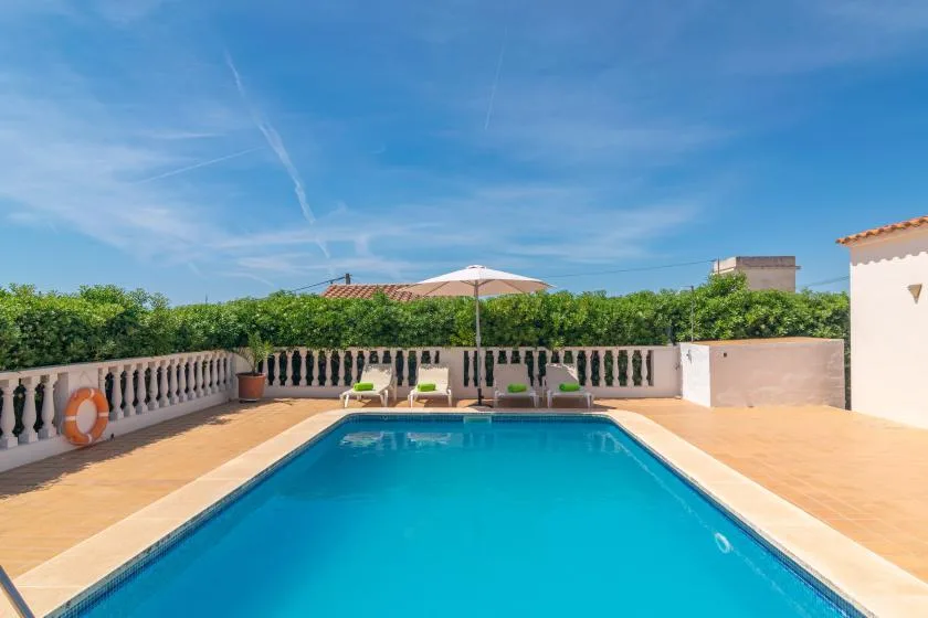 A swimming pool sits on a sunny terrace bordered by a balustrade and greenery.