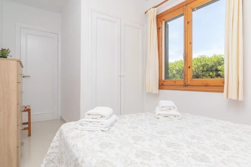A bright bedroom with a bed beneath a large wood-framed window.