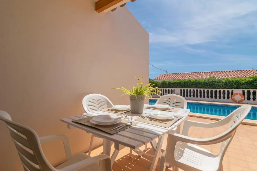 A sunny outdoor dining area with a table and seating beside a swimming pool.
