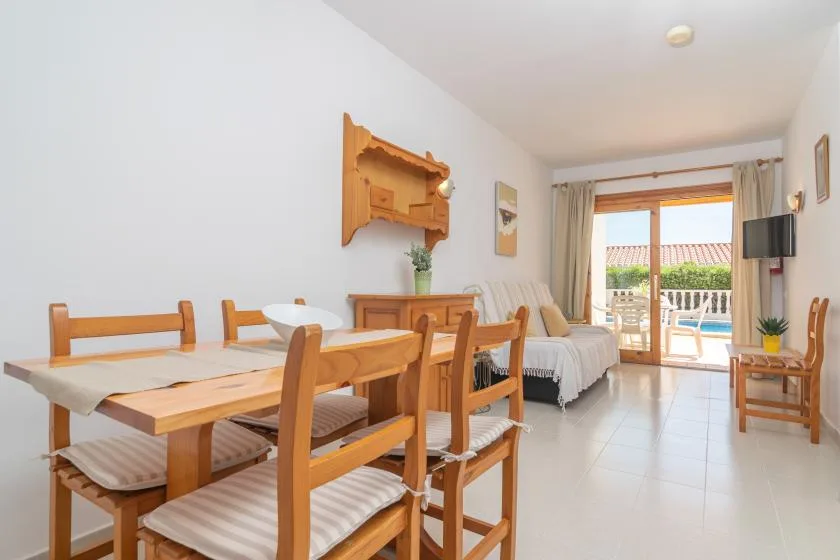 A bright living and dining room with a wooden dining table and seating beside a glass patio door.