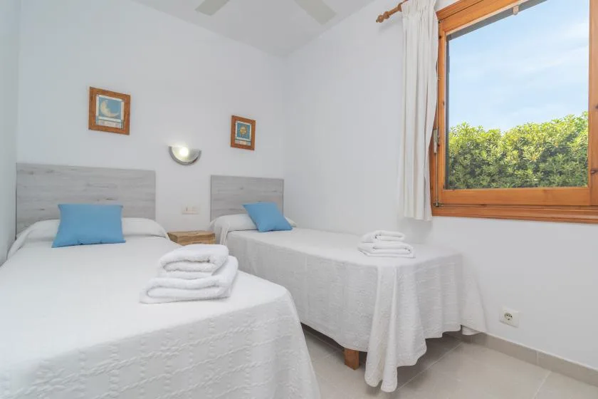 A bright bedroom with two beds and a large window overlooking greenery.