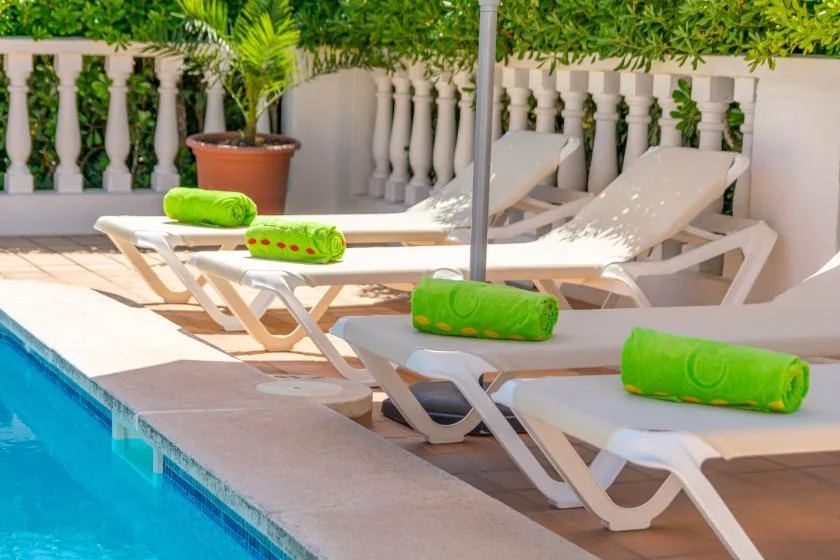Poolside loungers with bright green towels sit beside a turquoise swimming pool.