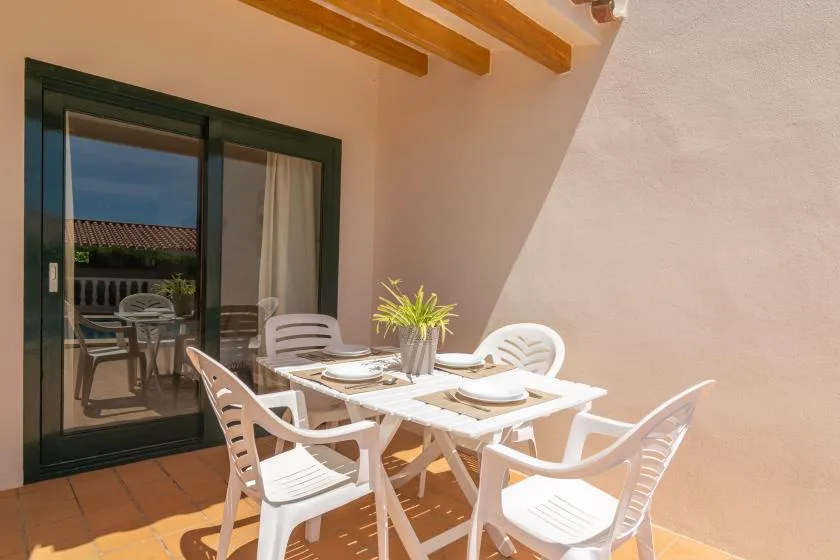 A sunlit outdoor dining area with a table and white seating beside a glass door.
