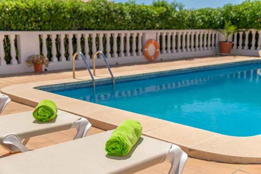 An outdoor swimming pool beside loungers, with green towels on the deck.