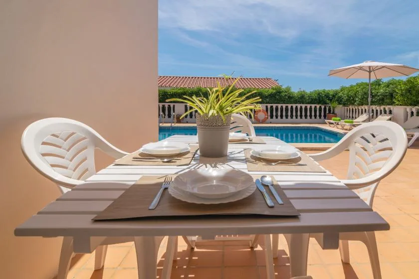 An outdoor dining area with a set table beside a swimming pool.