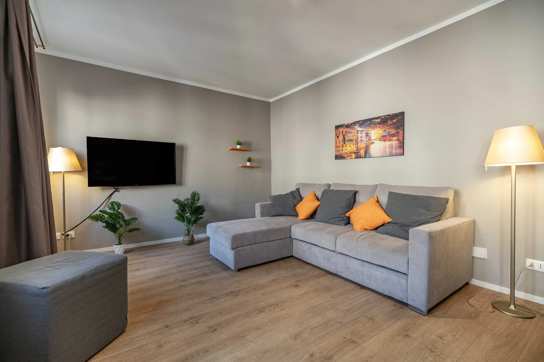 A living room with a gray sectional sofa, television, and floor lamps.