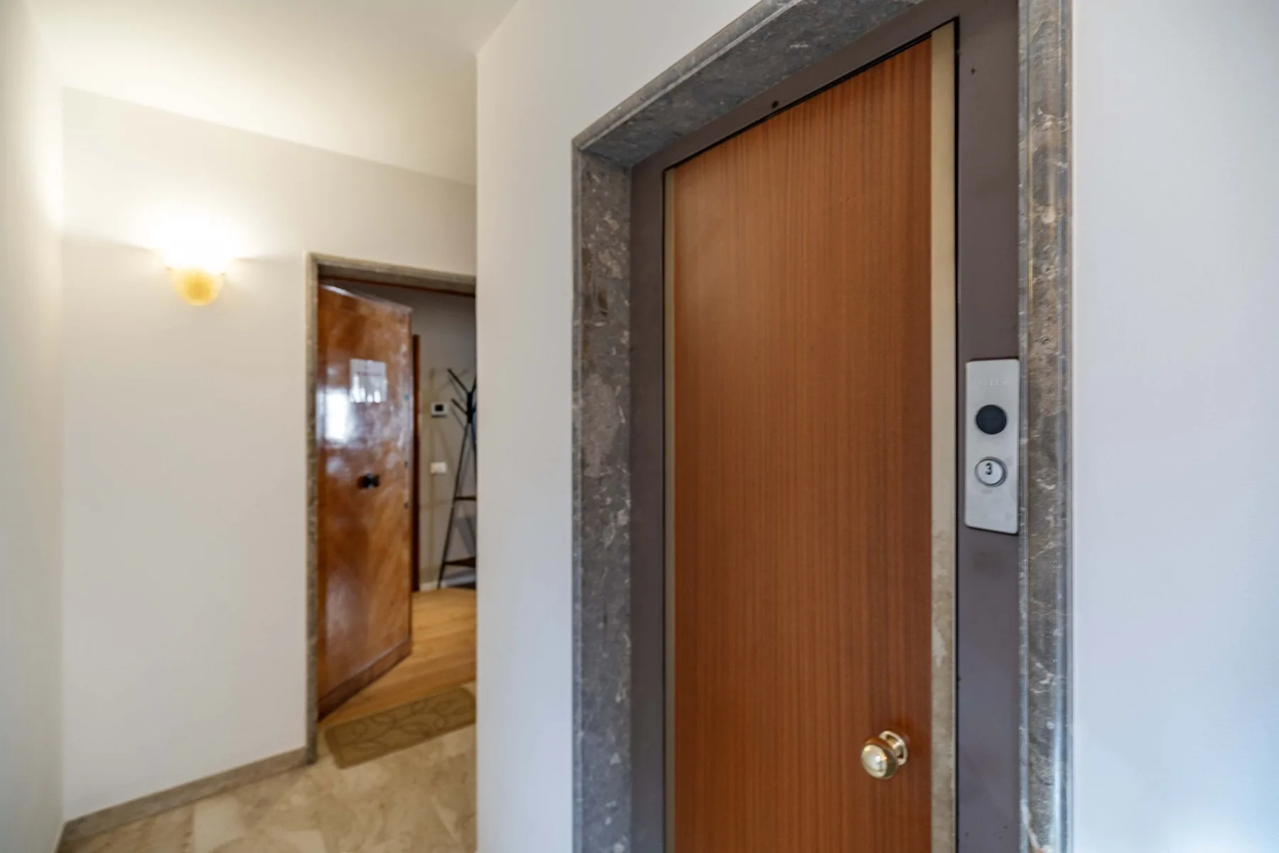 An interior hallway with a wooden door and a wall light.