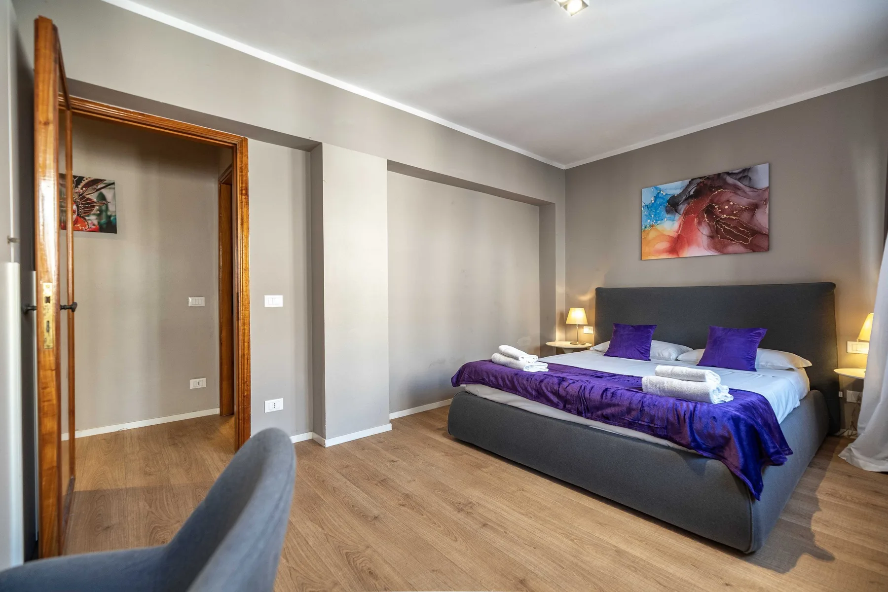 A bedroom with a bed dressed in purple bedding and bedside lamps.